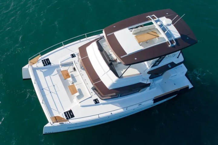 Aerial view of a white catamaran with a brown canopy on blue-green water.