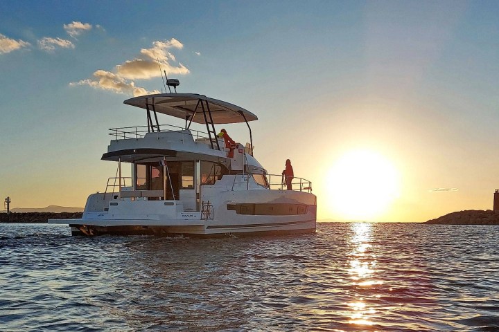 A boat sailing towards the sunset with calm ocean waters and a clear sky.