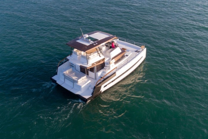 Aerial view of a white yacht with wooden deck cruising on blue sea.
