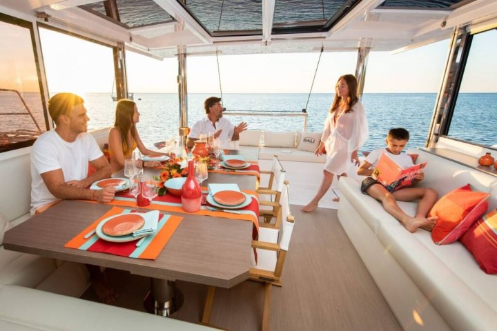 People enjoying a meal and reading on a boat with ocean view at sunset.